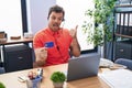 Young hispanic man wearing call center agent headset holding credit card pointing thumb up to the side smiling happy with open Royalty Free Stock Photo