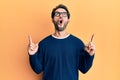 Young hispanic man wearing casual clothes and glasses amazed and surprised looking up and pointing with fingers and raised arms Royalty Free Stock Photo