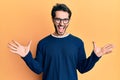 Young hispanic man wearing casual clothes and glasses celebrating victory with happy smile and winner expression with raised hands Royalty Free Stock Photo