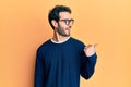 Young hispanic man wearing casual clothes and glasses smiling with happy face looking and pointing to the side with thumb up Royalty Free Stock Photo