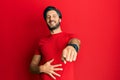 Young hispanic man wearing casual red t shirt laughing at you, pointing finger to the camera with hand over body, shame expression Royalty Free Stock Photo