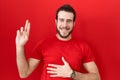 Young hispanic man wearing casual red t shirt smiling swearing with hand on chest and fingers up, making a loyalty promise oath Royalty Free Stock Photo