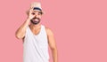 Young hispanic man wearing casual summer hat doing ok gesture with hand smiling, eye looking through fingers with happy face Royalty Free Stock Photo
