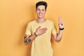 Young hispanic man wearing casual yellow t shirt smiling swearing with hand on chest and fingers up, making a loyalty promise oath Royalty Free Stock Photo