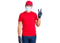 Young hispanic man wearing covid-19 safety mask smiling with happy face winking at the camera doing victory sign