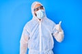 Young hispanic man wearing doctor coronavirus protection uniform smiling with happy face looking and pointing to the side with Royalty Free Stock Photo