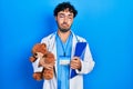 Young hispanic man wearing doctor uniform holding teddy bear and clipboard depressed and worry for distress, crying angry and Royalty Free Stock Photo