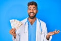 Young hispanic man wearing doctor uniform holding uk pounds banknotes celebrating achievement with happy smile and winner