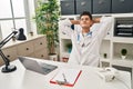 Young hispanic man wearing doctor uniform relaxed with hands on head at clinic Royalty Free Stock Photo