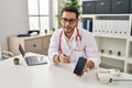 Young hispanic man wearing doctor uniform showing medical smartphone app at clinic