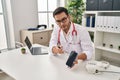 Young hispanic man wearing doctor uniform showing medical smartphone app at clinic