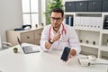 Young hispanic man wearing doctor uniform showing medical smartphone app at clinic