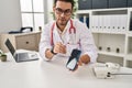 Young hispanic man wearing doctor uniform showing medical smartphone app at clinic