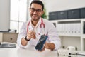 Young hispanic man wearing doctor uniform showing medical smartphone app at clinic