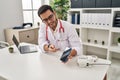 Young hispanic man wearing doctor uniform showing medical smartphone app at clinic