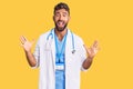 Young hispanic man wearing doctor uniform and stethoscope celebrating crazy and amazed for success with arms raised and open eyes Royalty Free Stock Photo