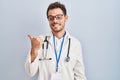 Young hispanic man wearing doctor uniform and stethoscope smiling with happy face looking and pointing to the side with thumb up Royalty Free Stock Photo