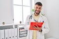 Young hispanic man wearing doctor uniform writing on clipboard at clinic Royalty Free Stock Photo