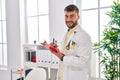 Young hispanic man wearing doctor uniform writing on clipboard at clinic Royalty Free Stock Photo