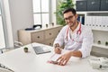 Young hispanic man wearing doctor uniform writing report working at clinic Royalty Free Stock Photo