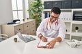 Young hispanic man wearing doctor uniform writing report working at clinic Royalty Free Stock Photo