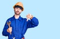 Young hispanic man wearing electrician uniform holding wrench with angry face, negative sign showing dislike with thumbs down, Royalty Free Stock Photo