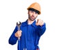 Young hispanic man wearing electrician uniform holding wrench pointing with finger to the camera and to you, confident gesture