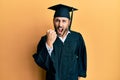 Young hispanic man wearing graduation cap and ceremony robe angry and mad raising fist frustrated and furious while shouting with Royalty Free Stock Photo