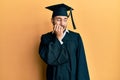 Young hispanic man wearing graduation cap and ceremony robe looking stressed and nervous with hands on mouth biting nails Royalty Free Stock Photo