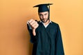 Young hispanic man wearing graduation cap and ceremony robe looking unhappy and angry showing rejection and negative with thumbs Royalty Free Stock Photo