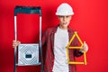 Young hispanic man wearing handyman uniform holding construction stairs and house project in shock face, looking skeptical and Royalty Free Stock Photo