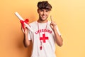 Young hispanic man wearing lifeguard t shirt using binoculars smiling with an idea or question pointing finger with happy face,