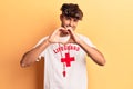 Young hispanic man wearing lifeguard t-shirt and whistle smiling in love doing heart symbol shape with hands
