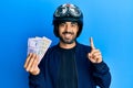 Young hispanic man wearing motorcycle helmet holding indian rupee smiling with an idea or question pointing finger with happy Royalty Free Stock Photo