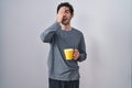 Young hispanic man wearing pajama drinking a cup of coffee yawning tired covering half face, eye and mouth with hand Royalty Free Stock Photo