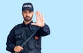 Young hispanic man wearing police uniform holding baton with open hand doing stop sign with serious and confident expression, Royalty Free Stock Photo