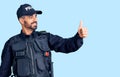 Young hispanic man wearing police uniform looking proud, smiling doing thumbs up gesture to the side