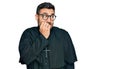 Young hispanic man wearing priest uniform looking stressed and nervous with hands on mouth biting nails