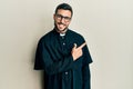 Young hispanic man wearing priest uniform standing over white background cheerful with a smile of face pointing with hand and Royalty Free Stock Photo