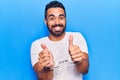 Young hispanic man wearing prisoner handcuffs smiling happy and positive, thumb up doing excellent and approval sign