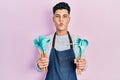 Young hispanic man wearing professional baker apron holding cooking tools making fish face with mouth and squinting eyes, crazy