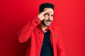 Young hispanic man wearing red leather jacket very happy and smiling looking far away with hand over head Royalty Free Stock Photo