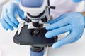 Young hispanic man wearing scientist gloves using microscope at laboratory