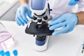 Young hispanic man wearing scientist gloves using microscope at laboratory