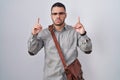 Young hispanic man wearing suitcase pointing up looking sad and upset, indicating direction with fingers, unhappy and depressed Royalty Free Stock Photo