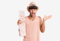 Young hispanic man wearing summer hat holding map celebrating victory with happy smile and winner expression with raised hands Royalty Free Stock Photo
