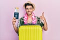 Young hispanic man wearing summer style and hawaiian lei holding passport and boarding pass smiling happy and positive, thumb up Royalty Free Stock Photo