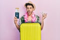 Young hispanic man wearing summer style and hawaiian lei holding passport and plane toy angry and mad screaming frustrated and Royalty Free Stock Photo