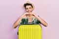 Young hispanic man wearing summer style and holding cabin bag smiling in love doing heart symbol shape with hands
