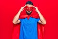 Young hispanic man wearing super hero costume with hand on head, headache because stress